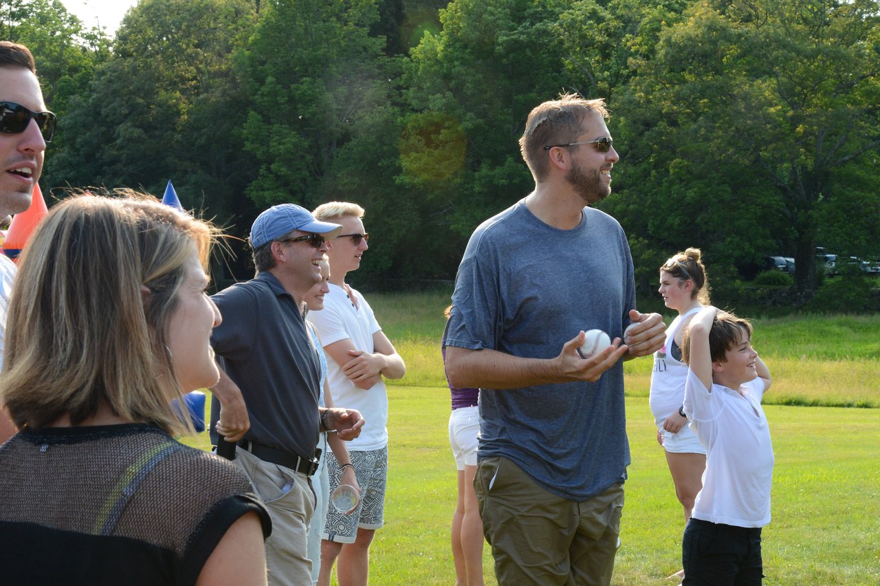 A man in a wet shirt holds a ball, preparing to throw, while a crowd watches and smiles.