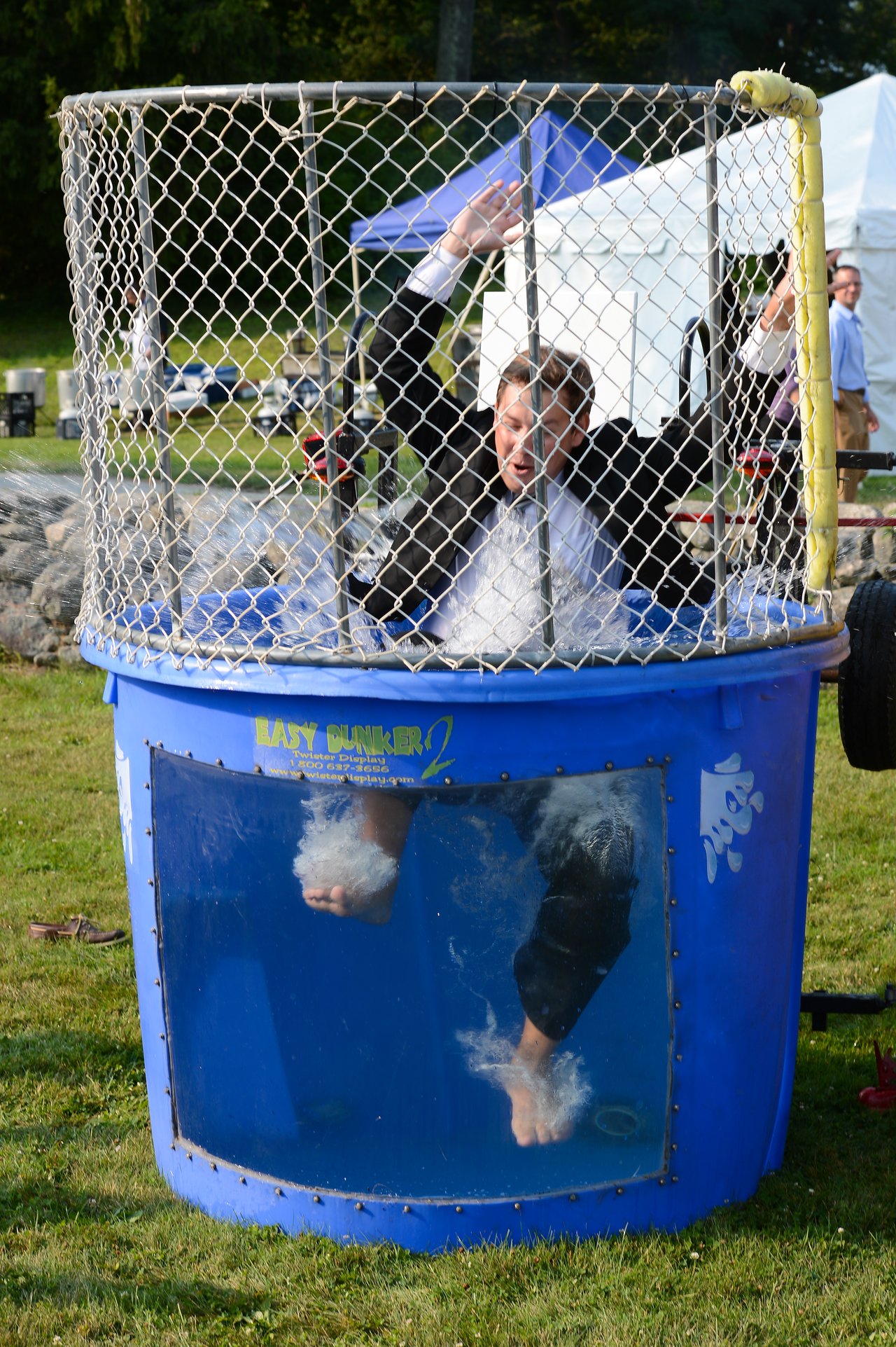 A man in a suit falls into a dunk tank, splashing water as he raises his arms.