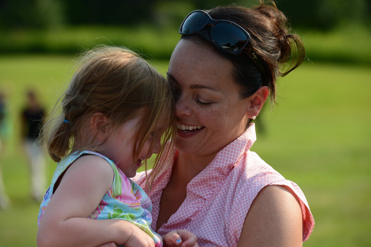 A woman smiles while holding a young girl in her arms at an outdoor event.