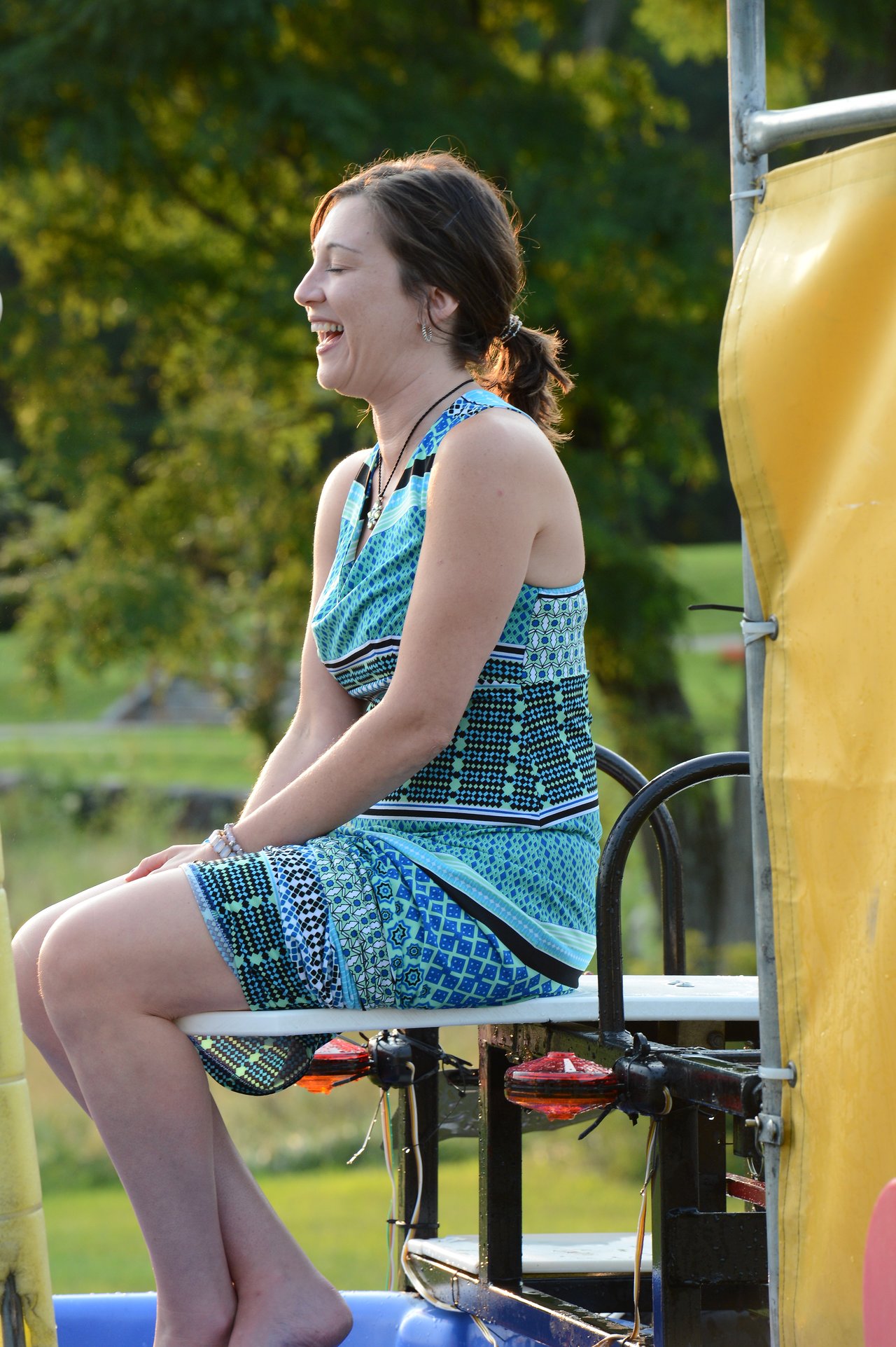 A woman sits on a dunk tank platform, smiling and waiting to be dropped into the water.