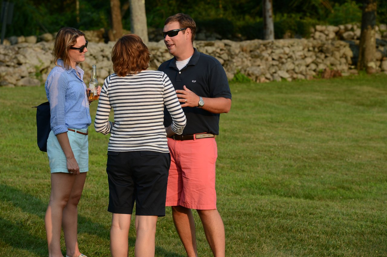 Three people stand on a grassy lawn, chatting.