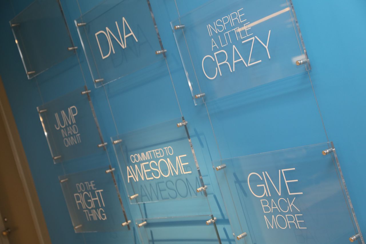 A blue wall features transparent plaques with motivational phrases like "DNA", "Inspire a little crazy", and "Give back more.