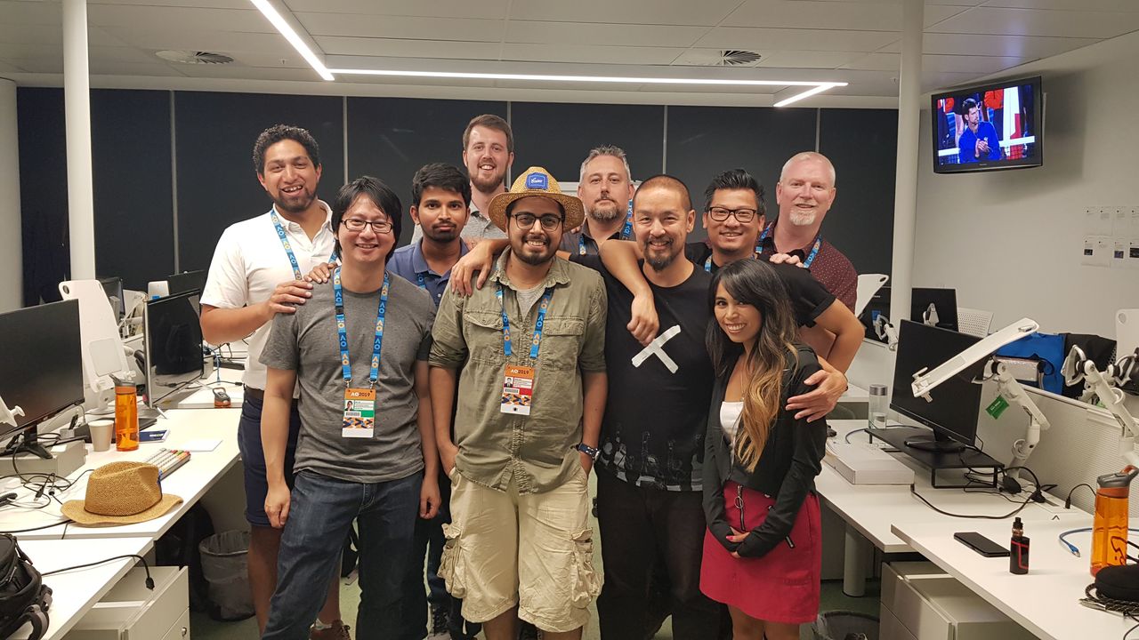 A group of ten people wearing event badges pose together in an office, smiling at the camera.