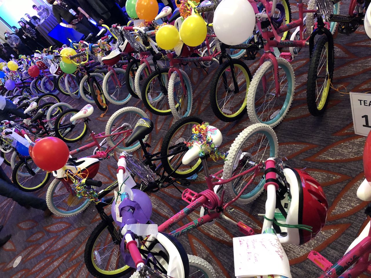 Rows of newly assembled children's bikes with balloons and helmets displayed indoors after a bike-building event.