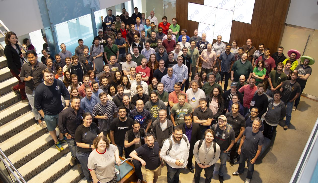 A large group of people posing together for a group photo at an Acquia Buildweek event indoors.