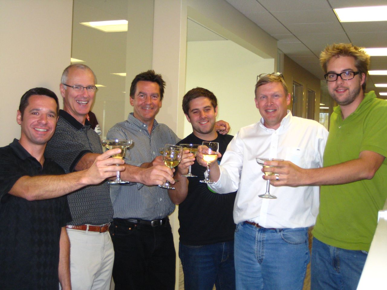 A group of six people smiling and raising glasses in a toast, celebrating the Drupal Commons release.