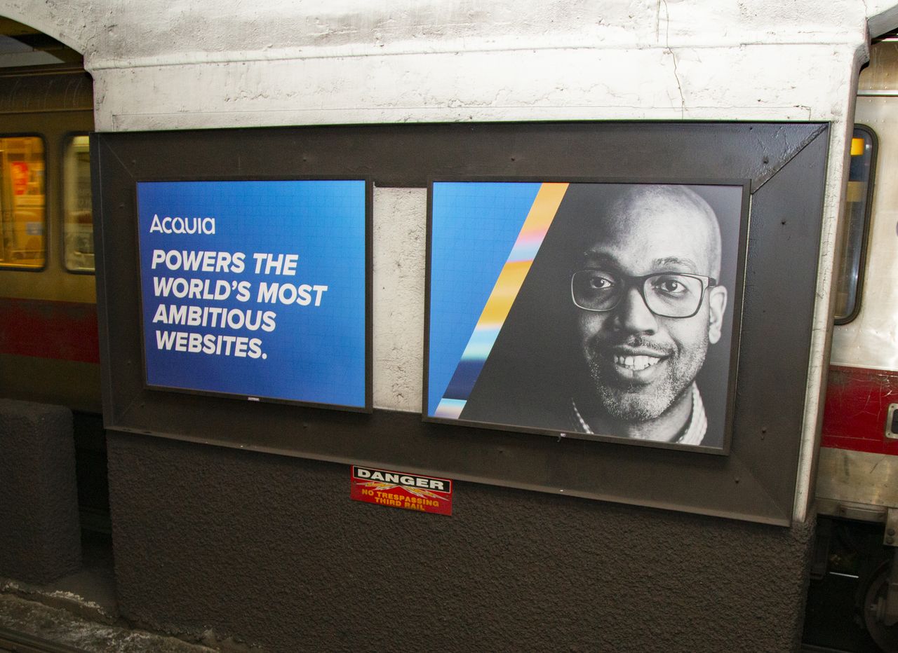 Two Acquia advertisements at a subway station, one with text about websites and another showing a smiling person.