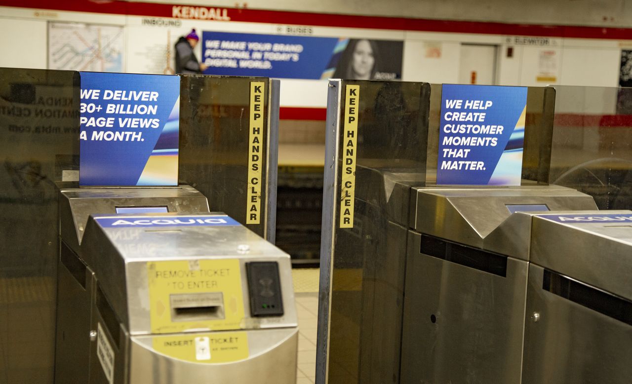 Turnstiles at Kendall Square station display Acquia advertisements about page views and customer engagement.