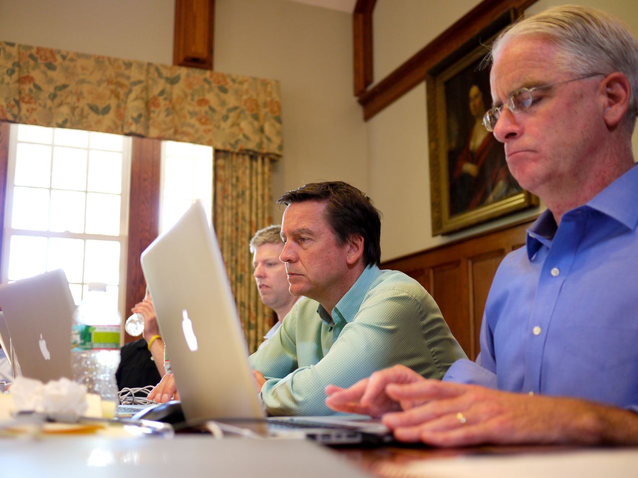 People in a meeting room working on laptops, engaged in discussion during a leadership offsite event.