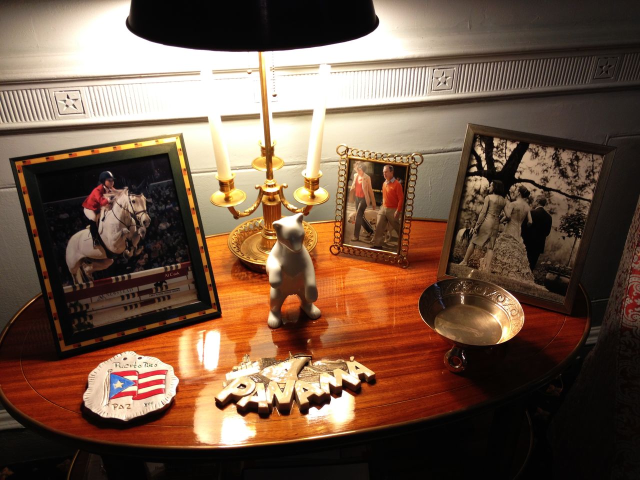 A wooden table with framed photographs, a lamp, a Puerto Rico plaque, a dog figurine, and decorative items.