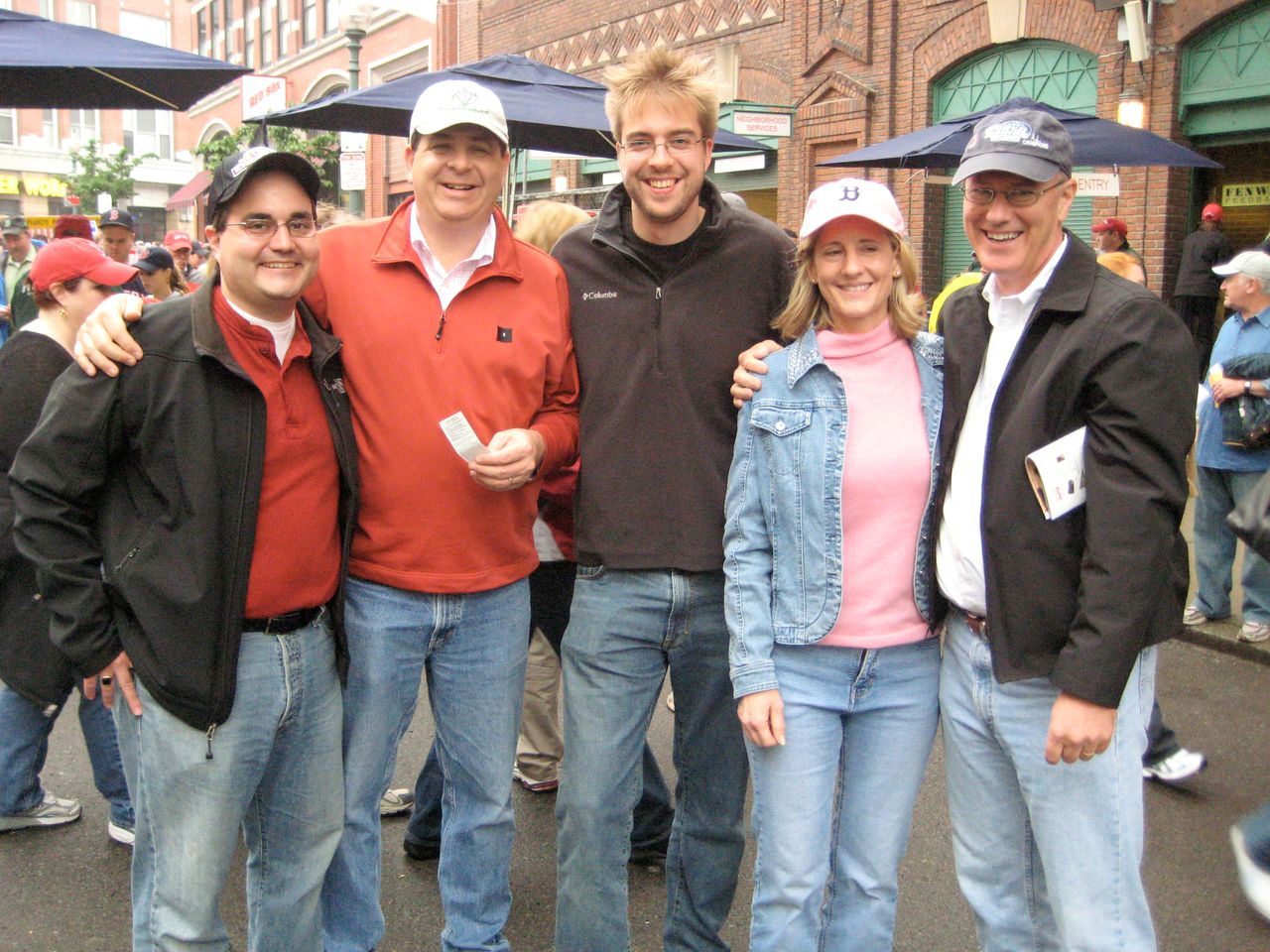 Five people smiling and posing outside a stadium, holding tickets before a Red Sox game.