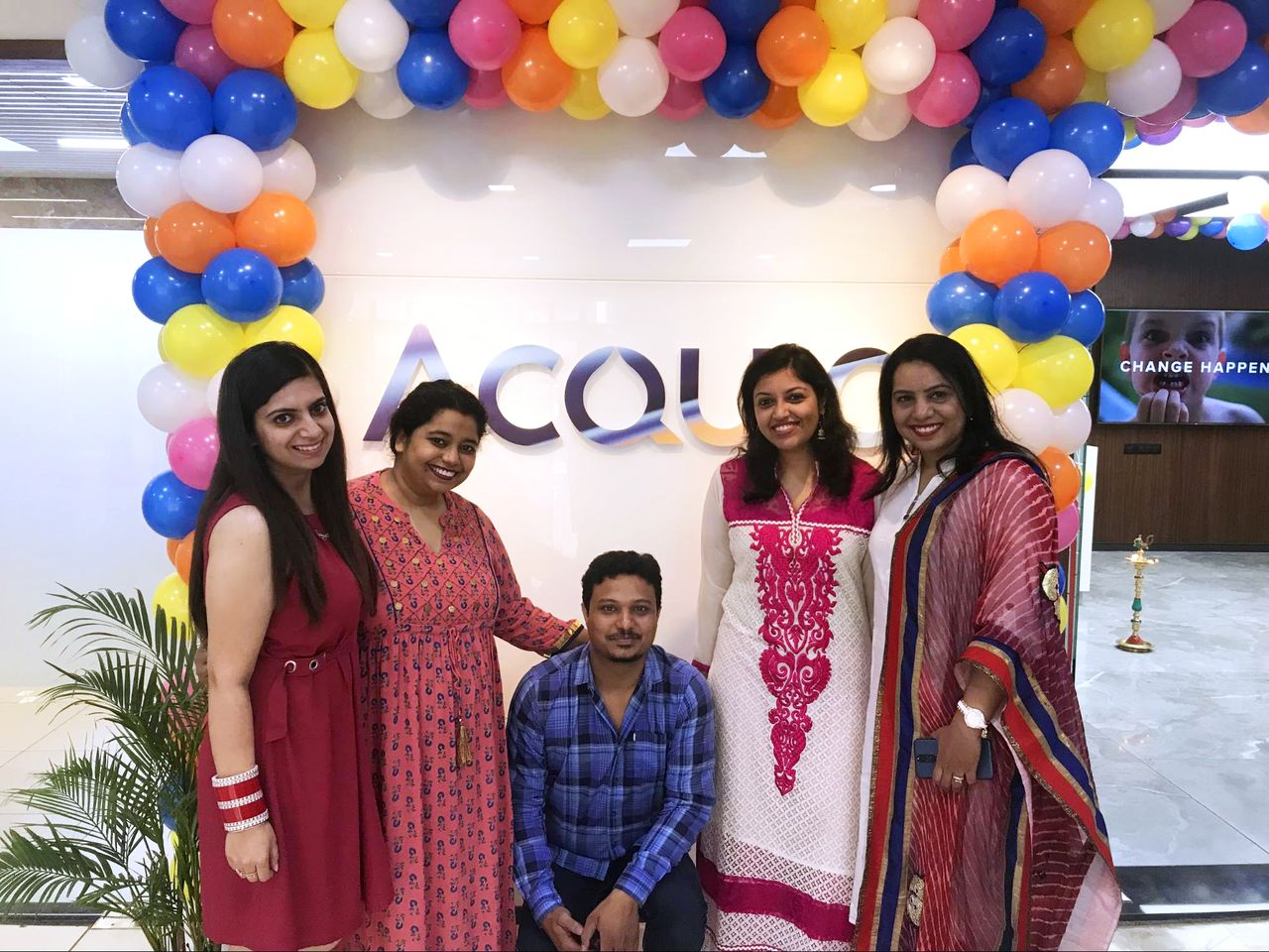 Five people posing in front of an "Acquia" sign with colorful balloons at the Pune, India office.