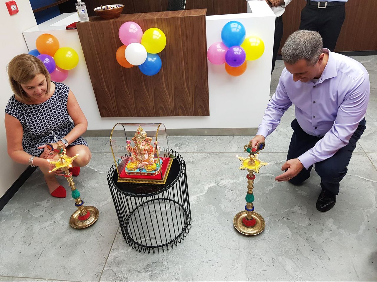 Two people light traditional brass lamps near a Ganesh idol during an office celebration in Pune, India.