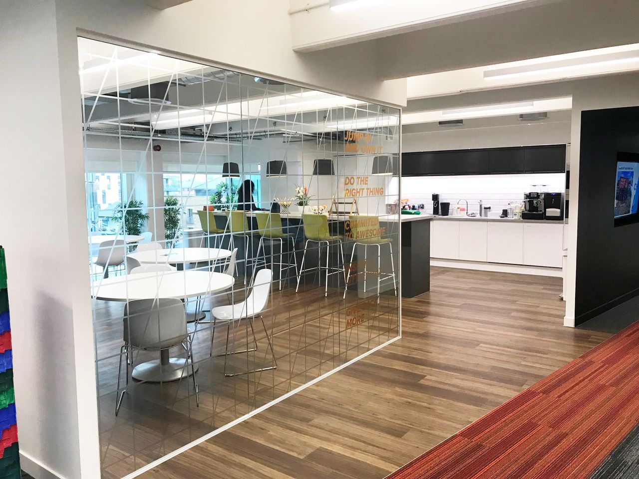 A modern office kitchen with seating area, glass partition, and motivational text.