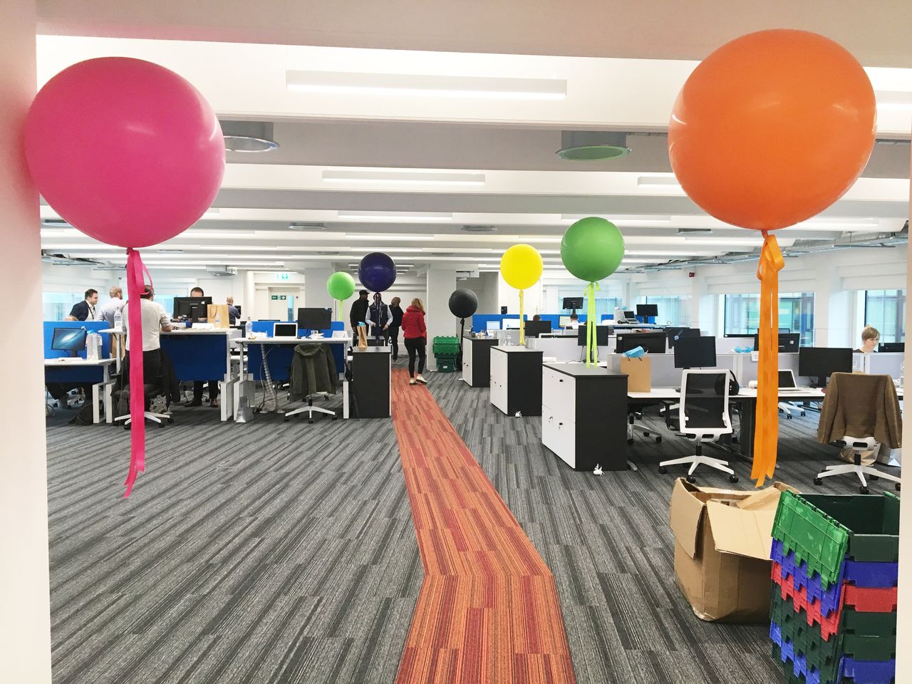 An open office space with desks, computers, and large colorful balloons tied to furniture and pillars.