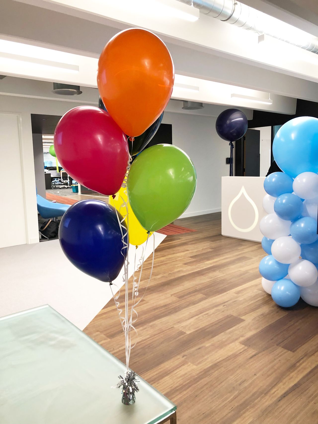Colorful balloons tied to a small weight on a glass table in an office space.