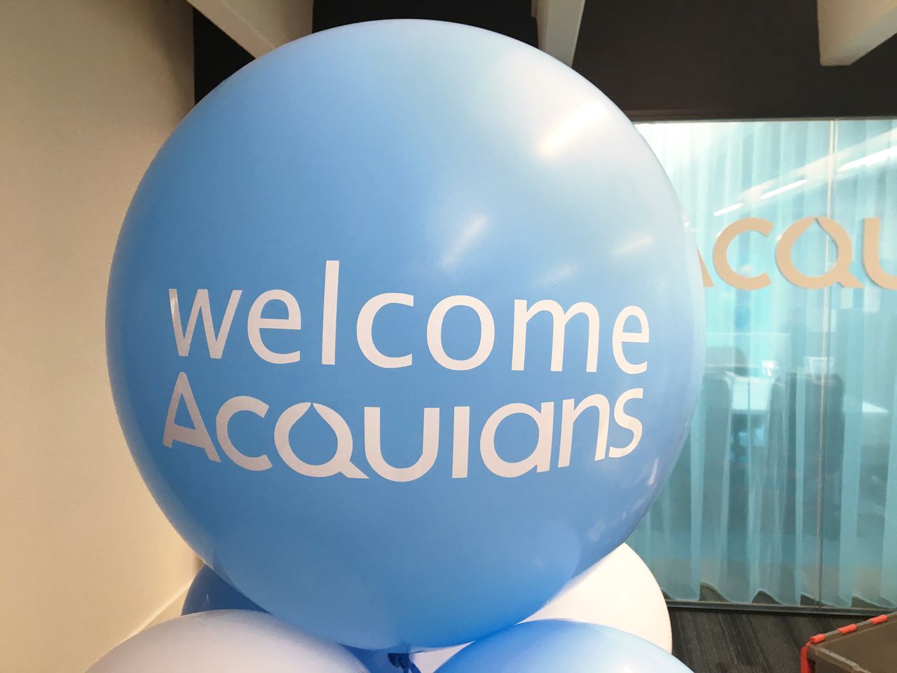 A large blue balloon with "Welcome Acquians" printed on it, placed in an office environment.