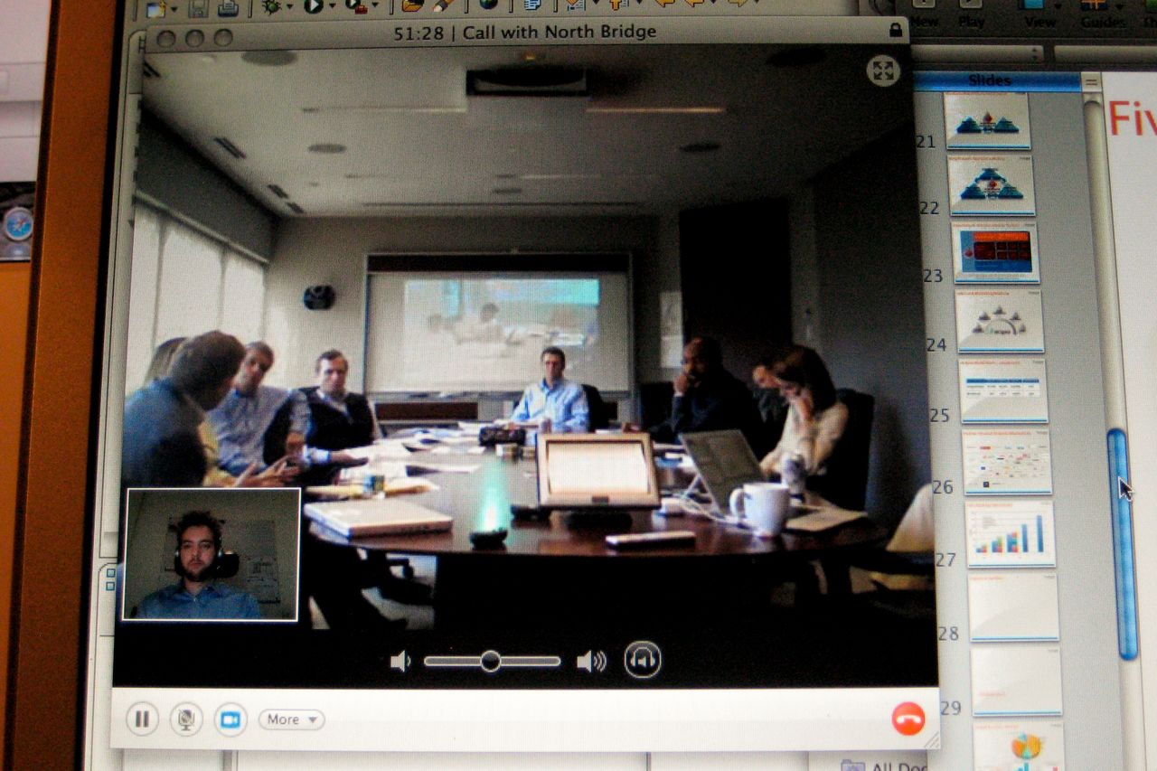 A video call shows a business meeting where people discuss fundraising, with presentation slides visible on the screen.