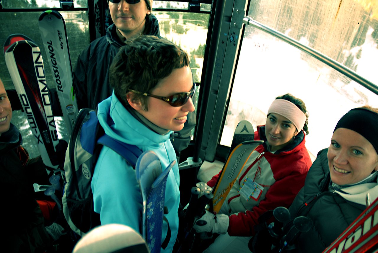 A group of skiers in winter gear ride a gondola, holding skis and poles, preparing for the slopes.