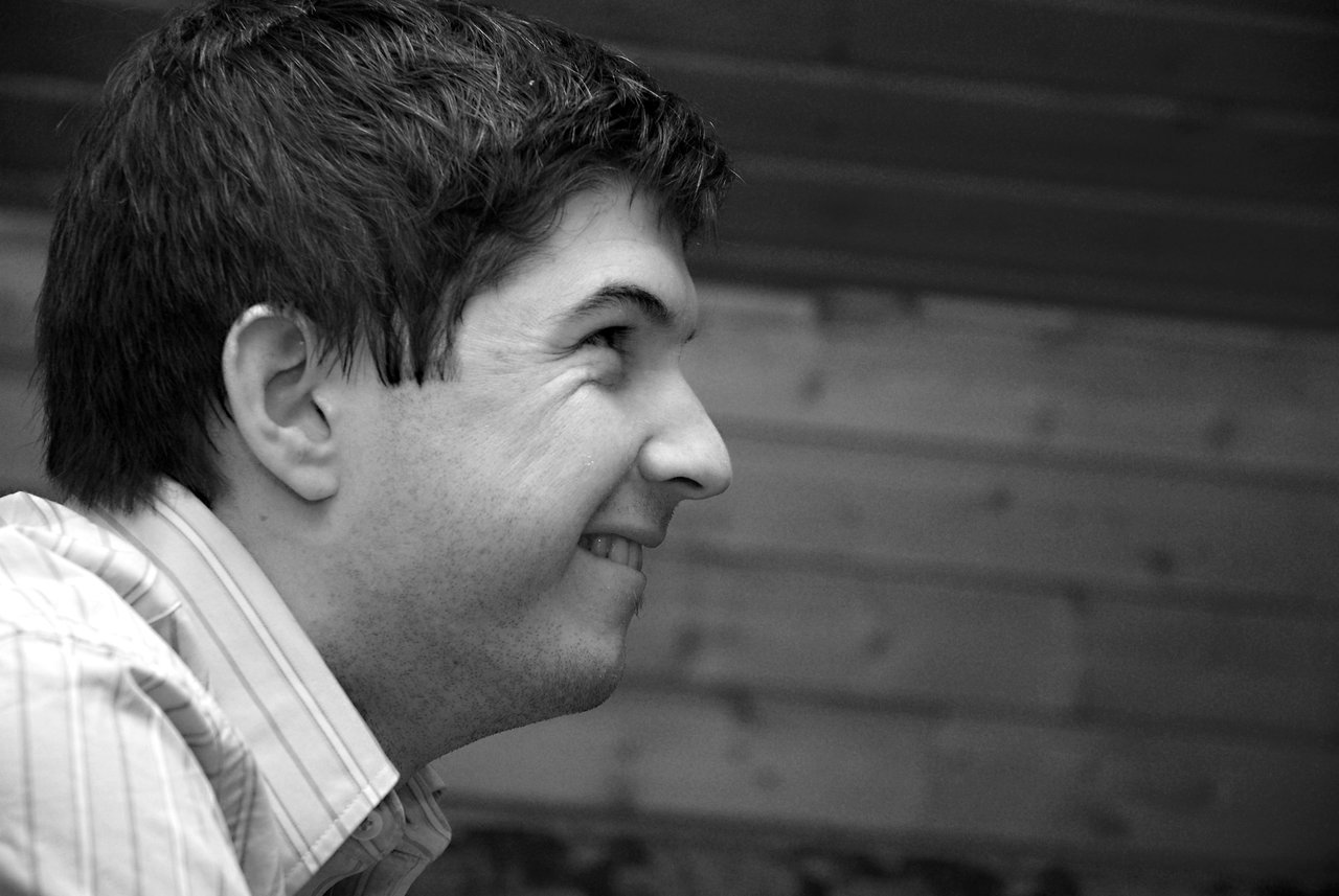 A man in a striped shirt smiles while looking to the side in a black-and-white photo.