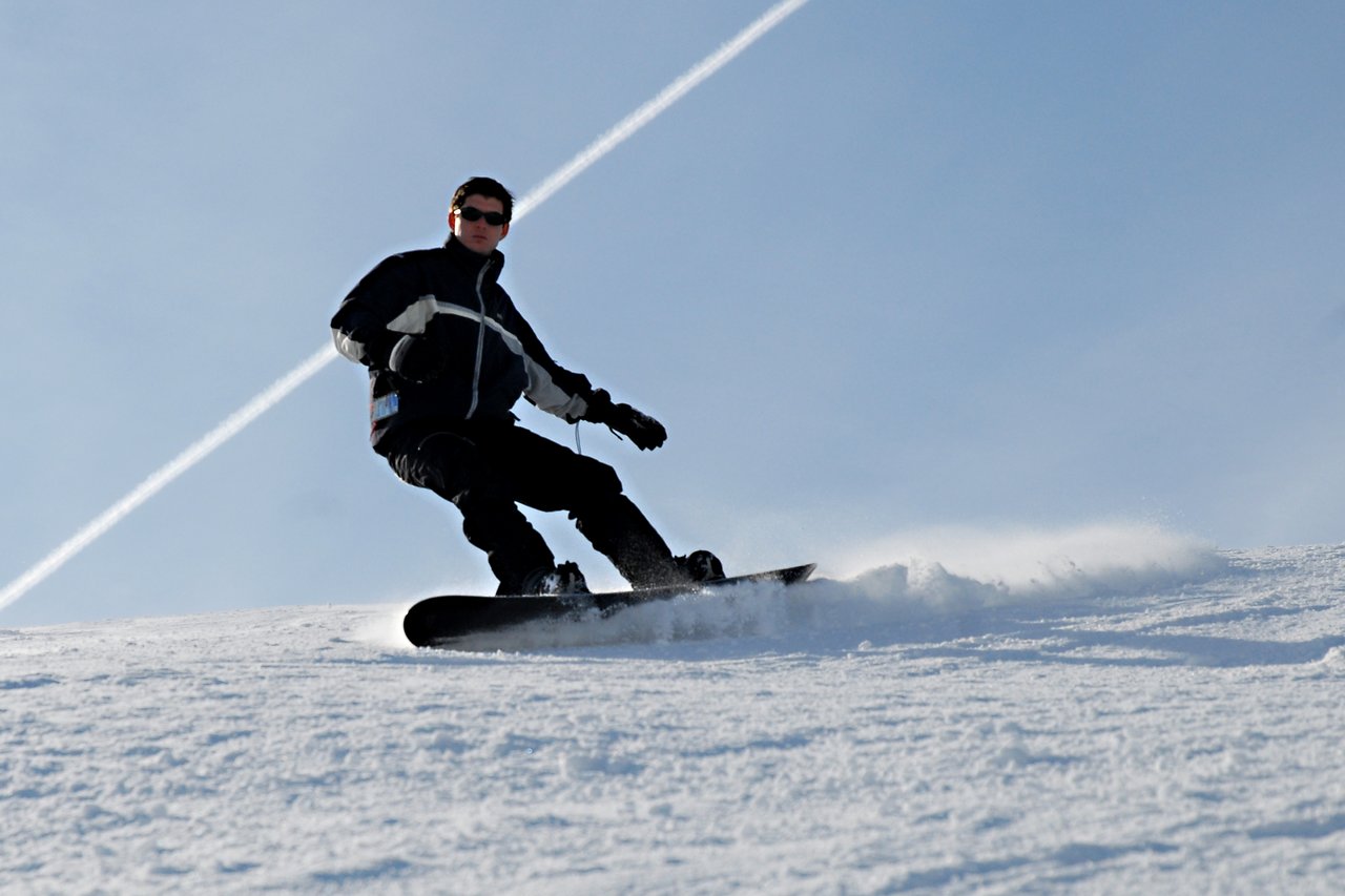 A person wearing a black and white jacket snowboards down a snowy slope, kicking up powder.