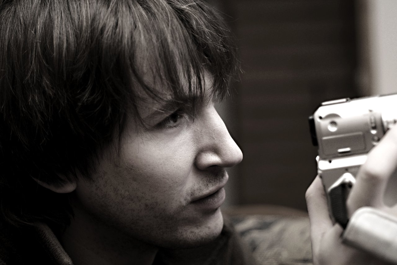 A person closely examines a handheld video camera, focusing on the viewfinder while holding it steadily.