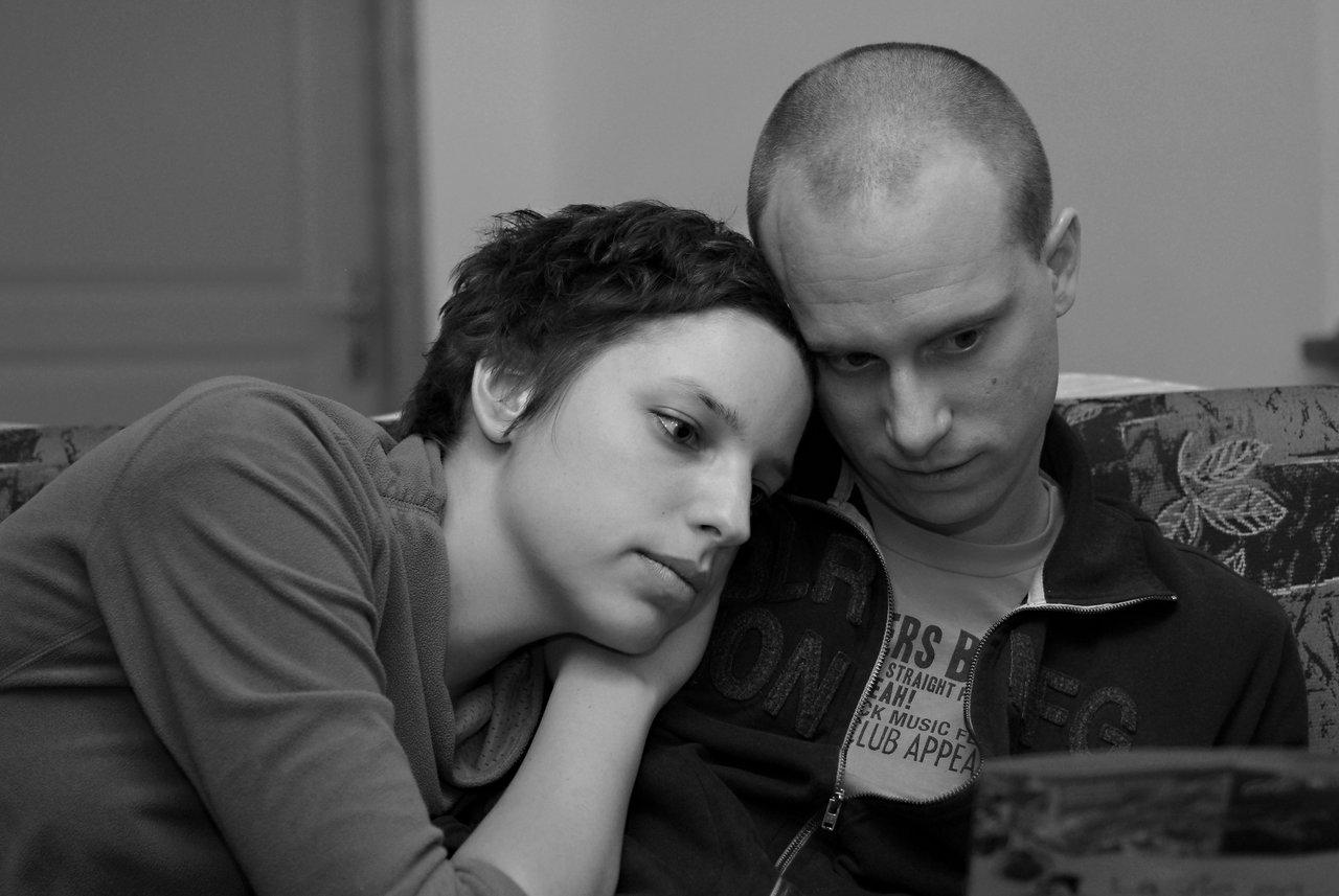 A woman leans her head on a man's shoulder as they both look at something in front of them.