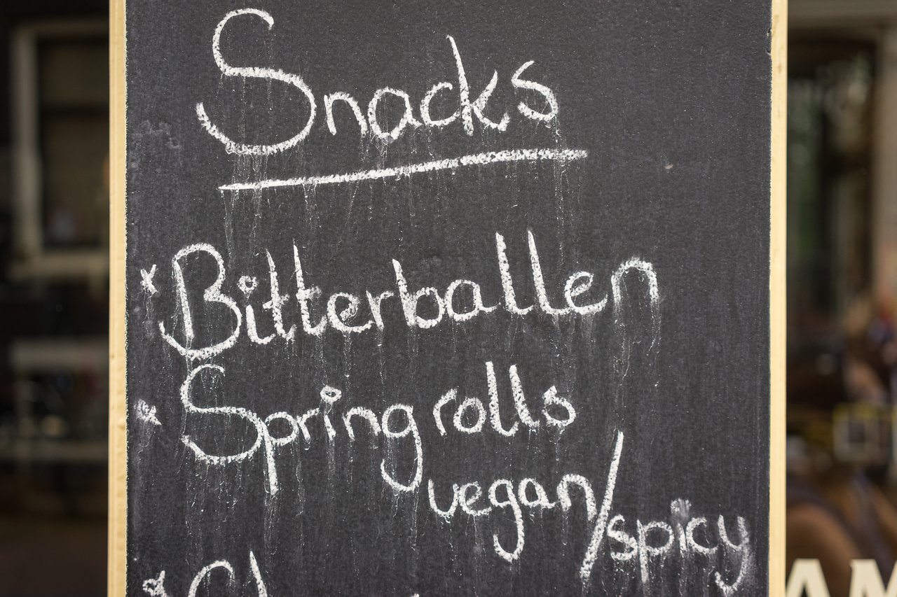 A chalkboard menu lists snacks, including bitterballen and vegan or spicy spring rolls.