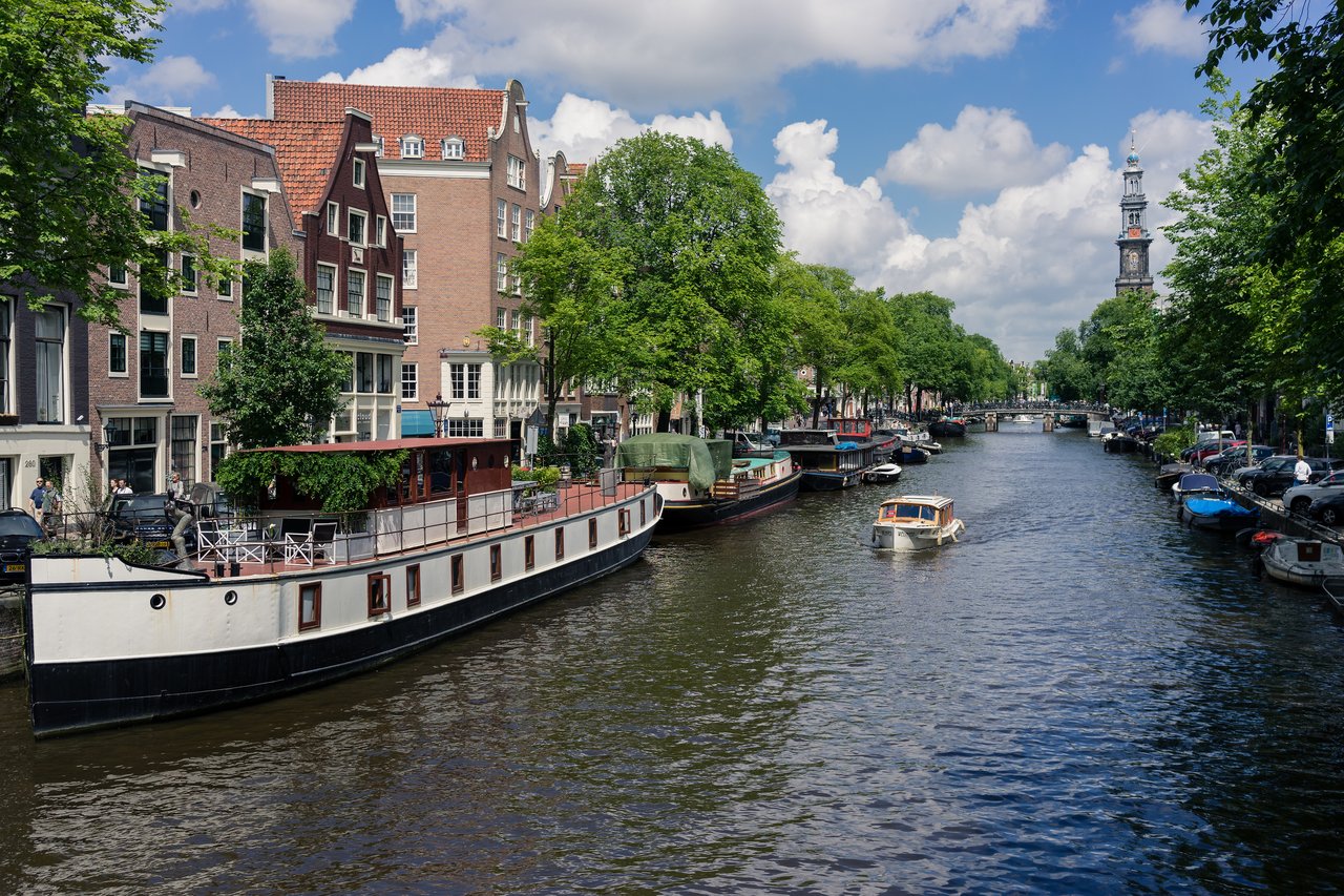 A canal in Amsterdam with houseboats, a small motorboat, and traditional buildings lining the water.