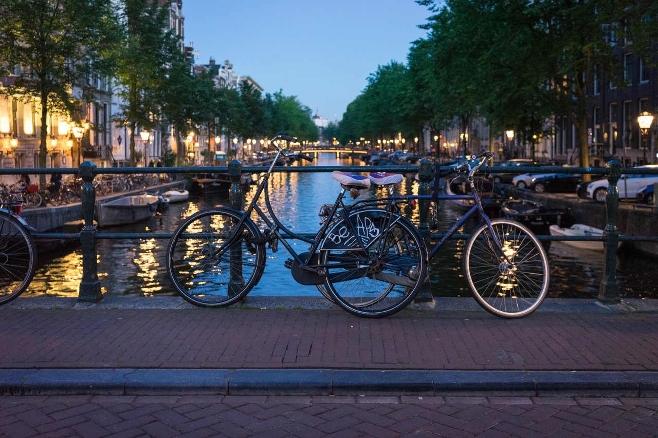 A bicycle leans against a railing on a canal bridge at night, with streetlights reflecting on the water.