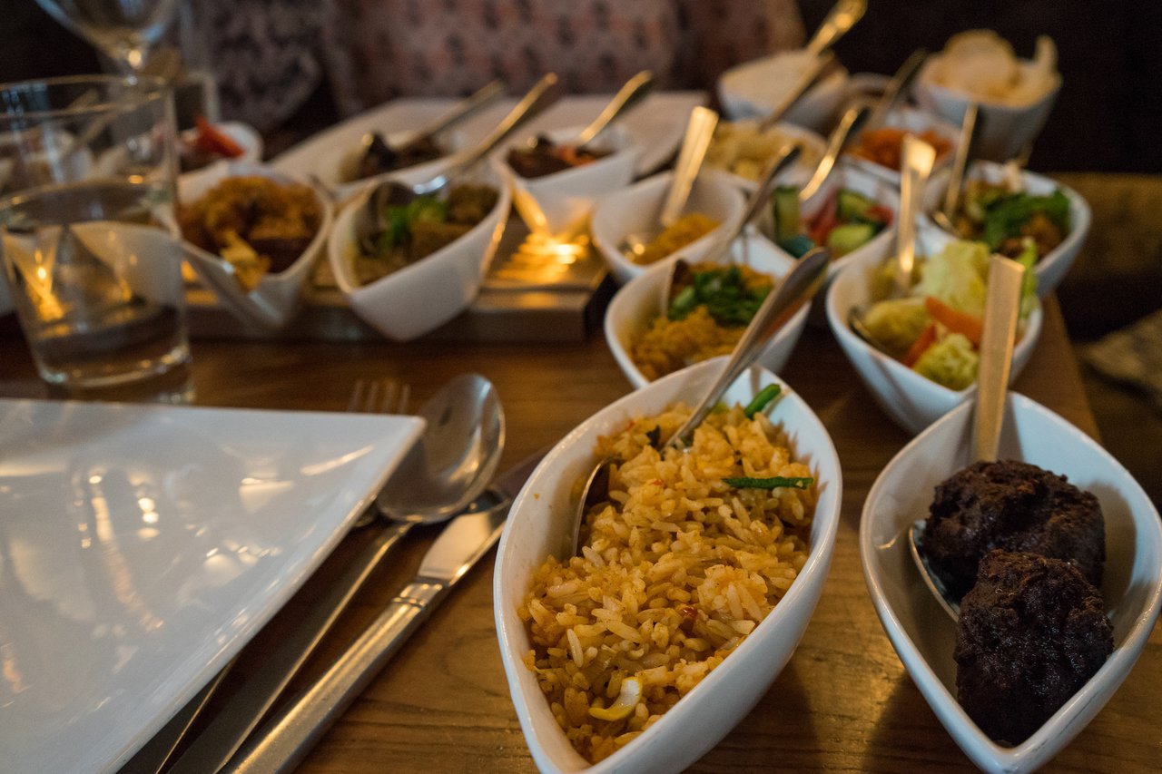 A table with multiple small dishes of Indonesian food, including rice, vegetables, and meat, served at a restaurant.