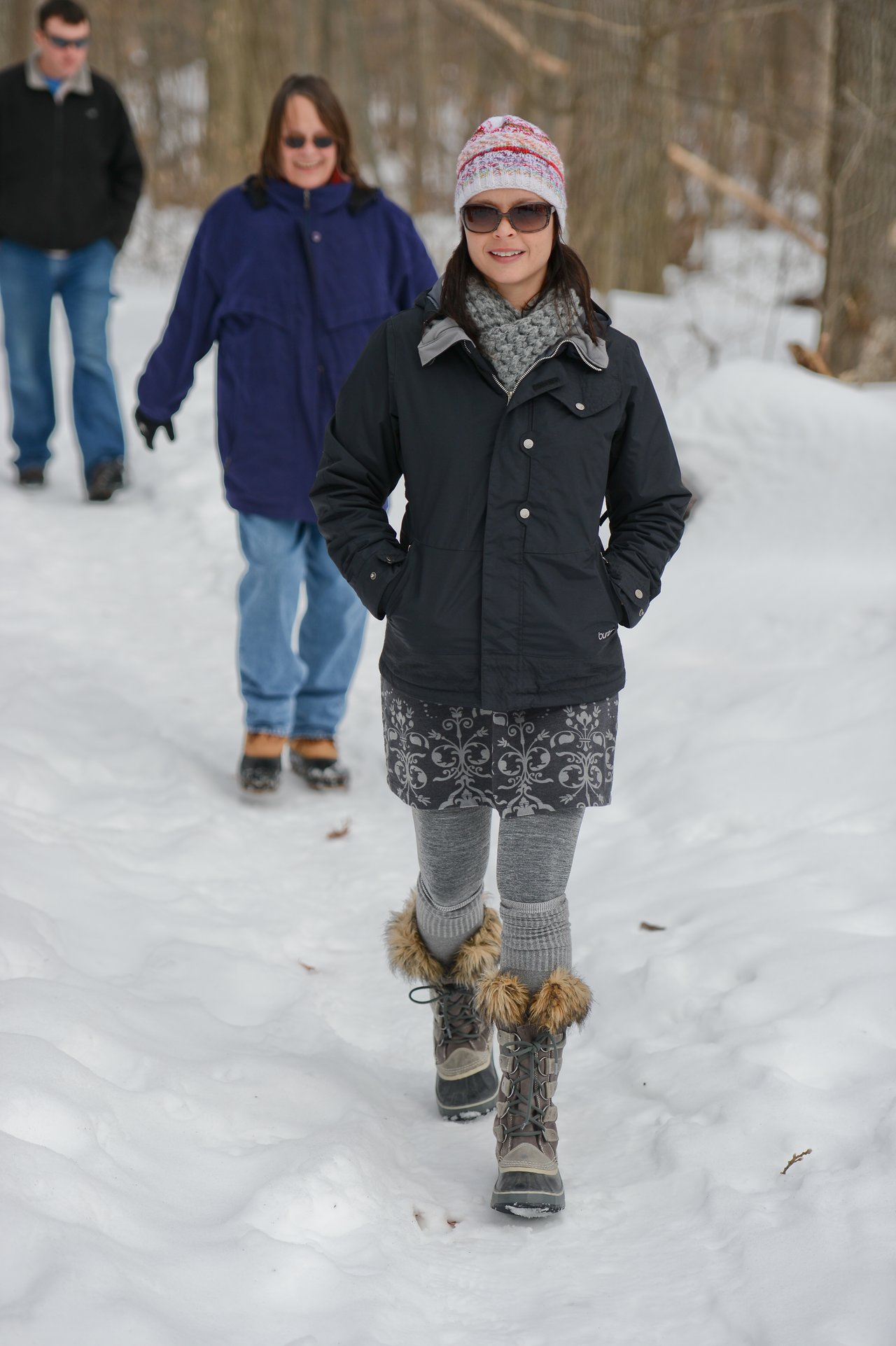 A woman in winter clothing walks on a snowy path, followed by two people dressed for cold weather.