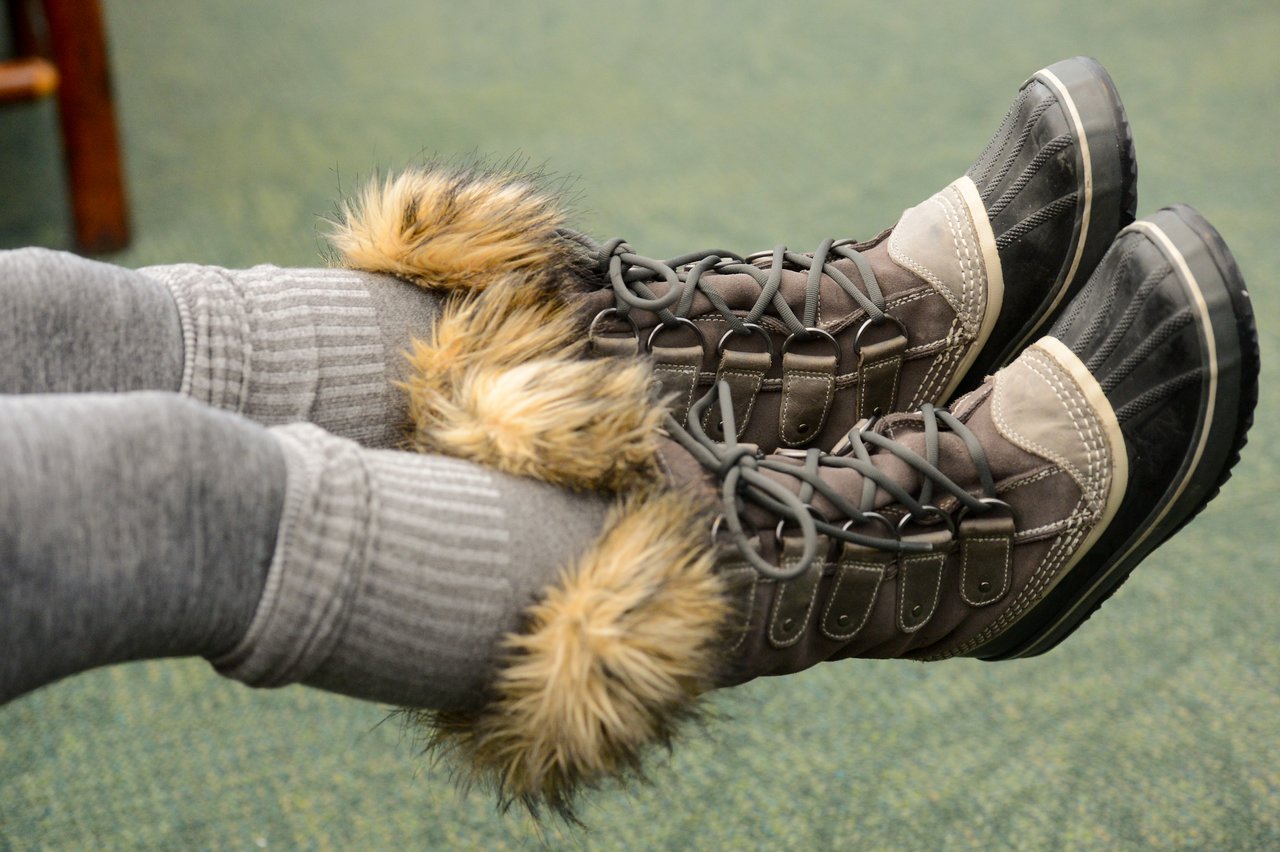 A person wearing gray leggings and fur-lined winter boots rests their feet in the air.