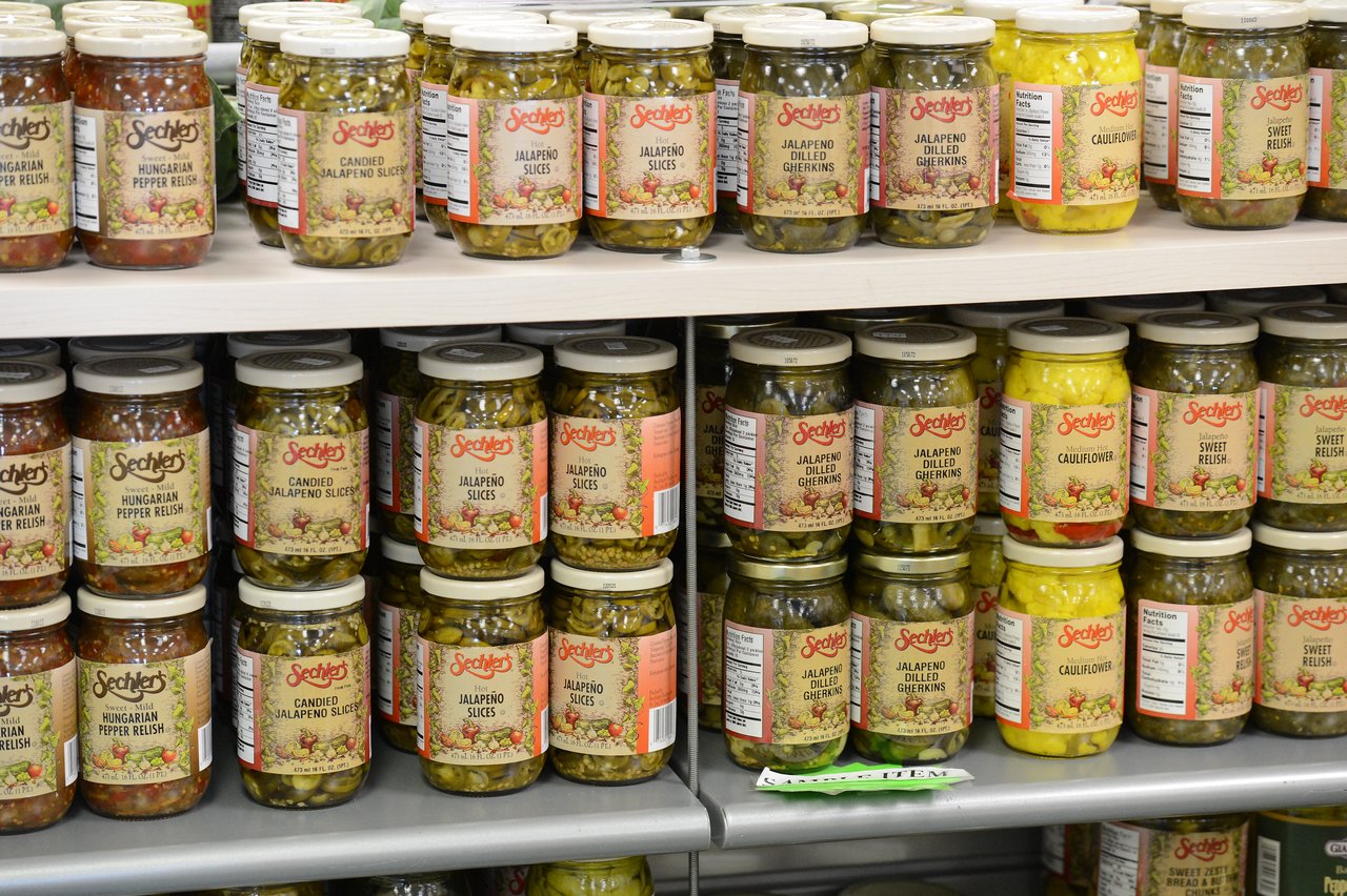 Jars of pickled vegetables and relishes neatly arranged on store shelves, including jalapeños, cauliflower, and pepper relish.
