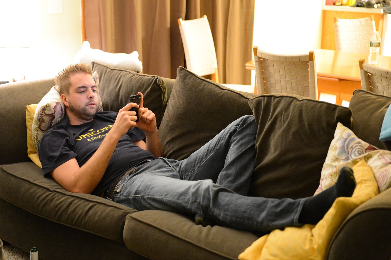 A man is lying on a couch, looking at his phone with a relaxed posture.