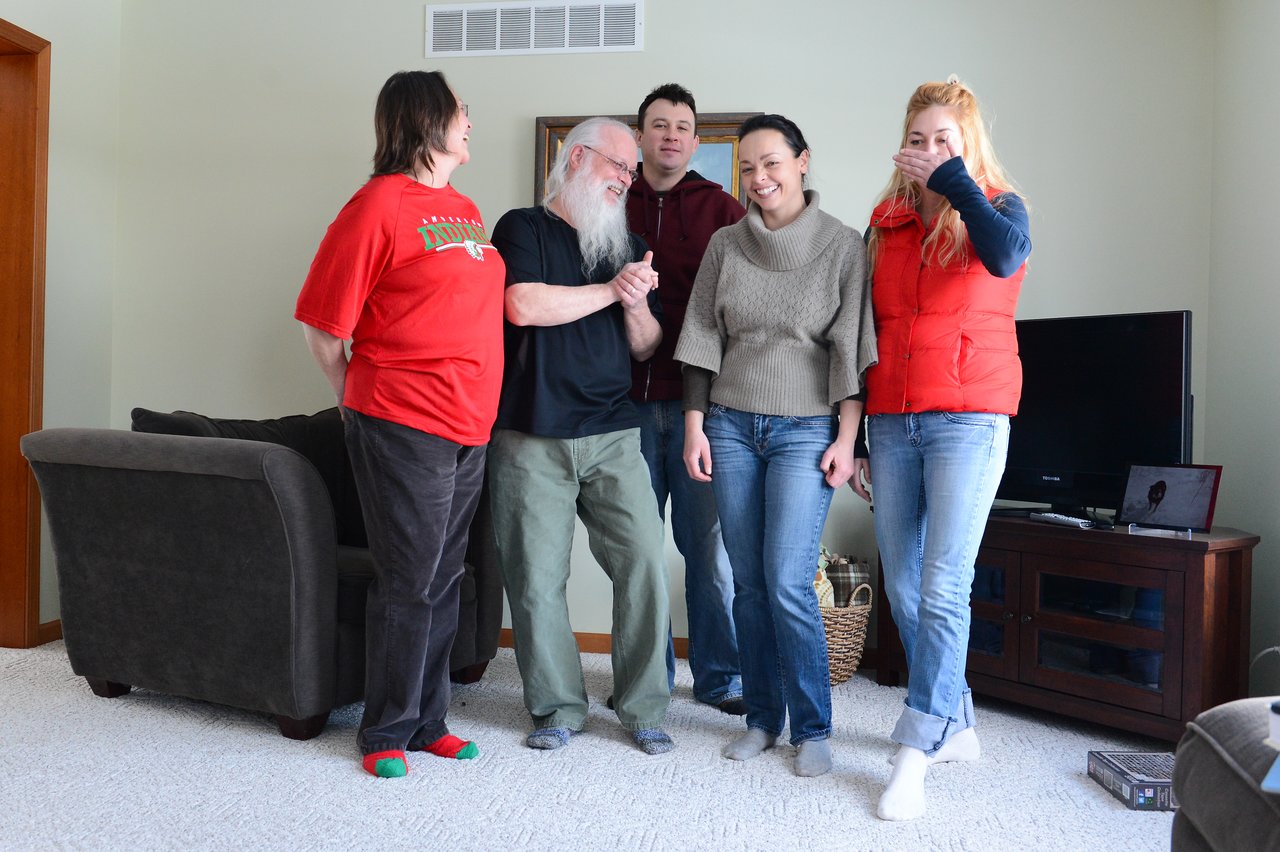 Five people stand in a living room, smiling and laughing together.