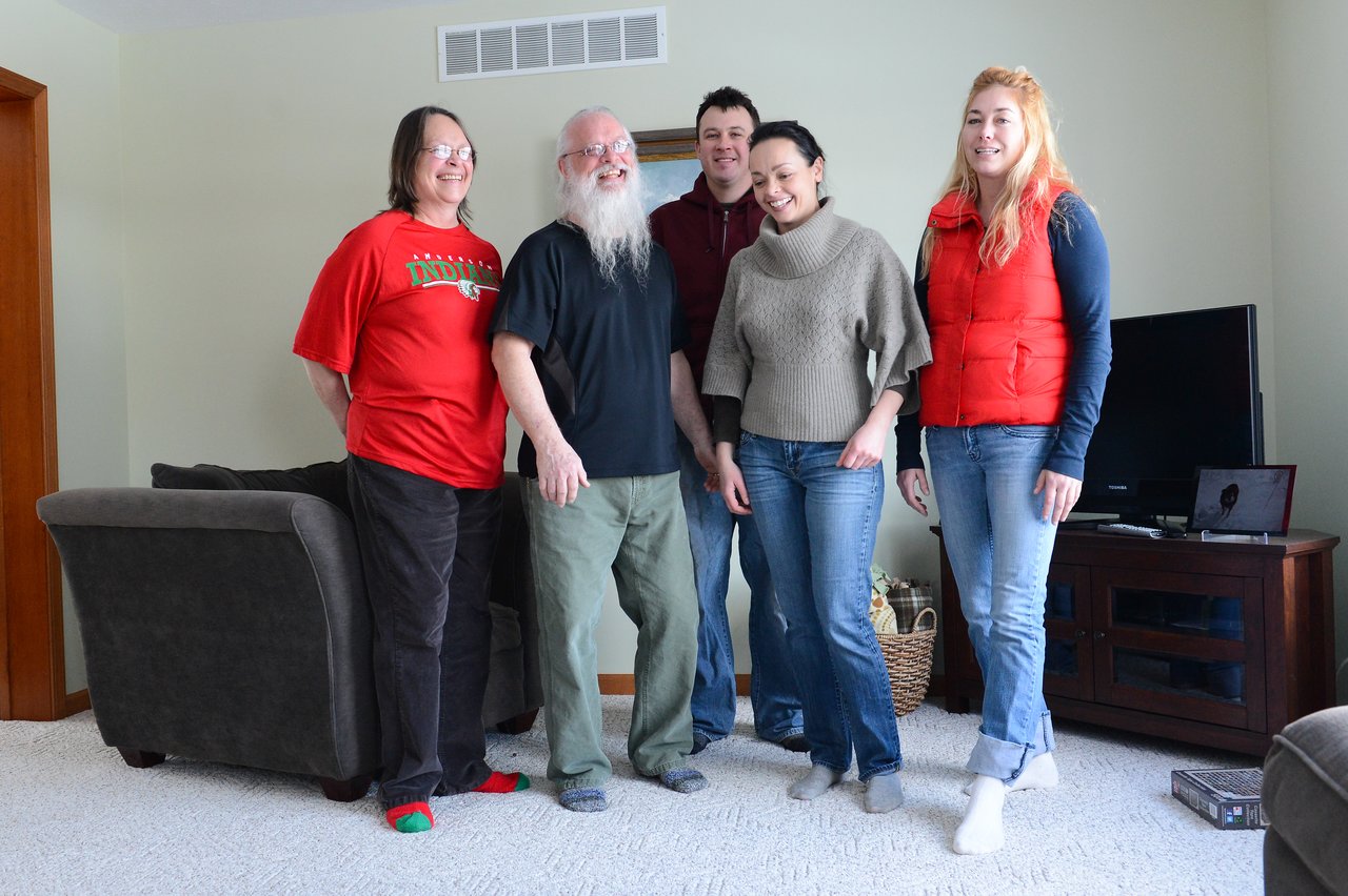 Five people stand together in a living room, smiling at the camera.