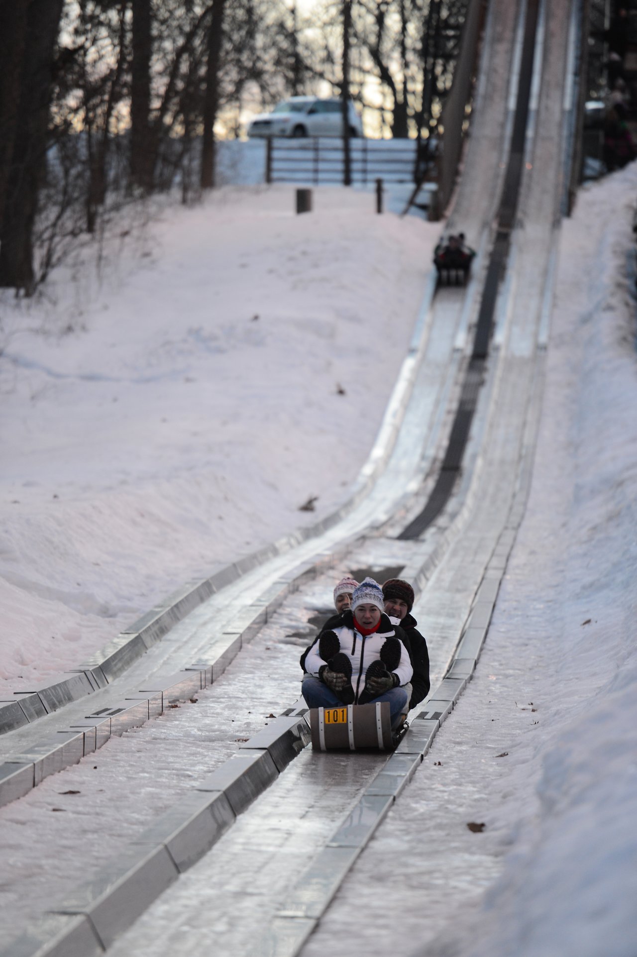 Three people ride a toboggan down an icy track, dressed in winter clothing and hats.