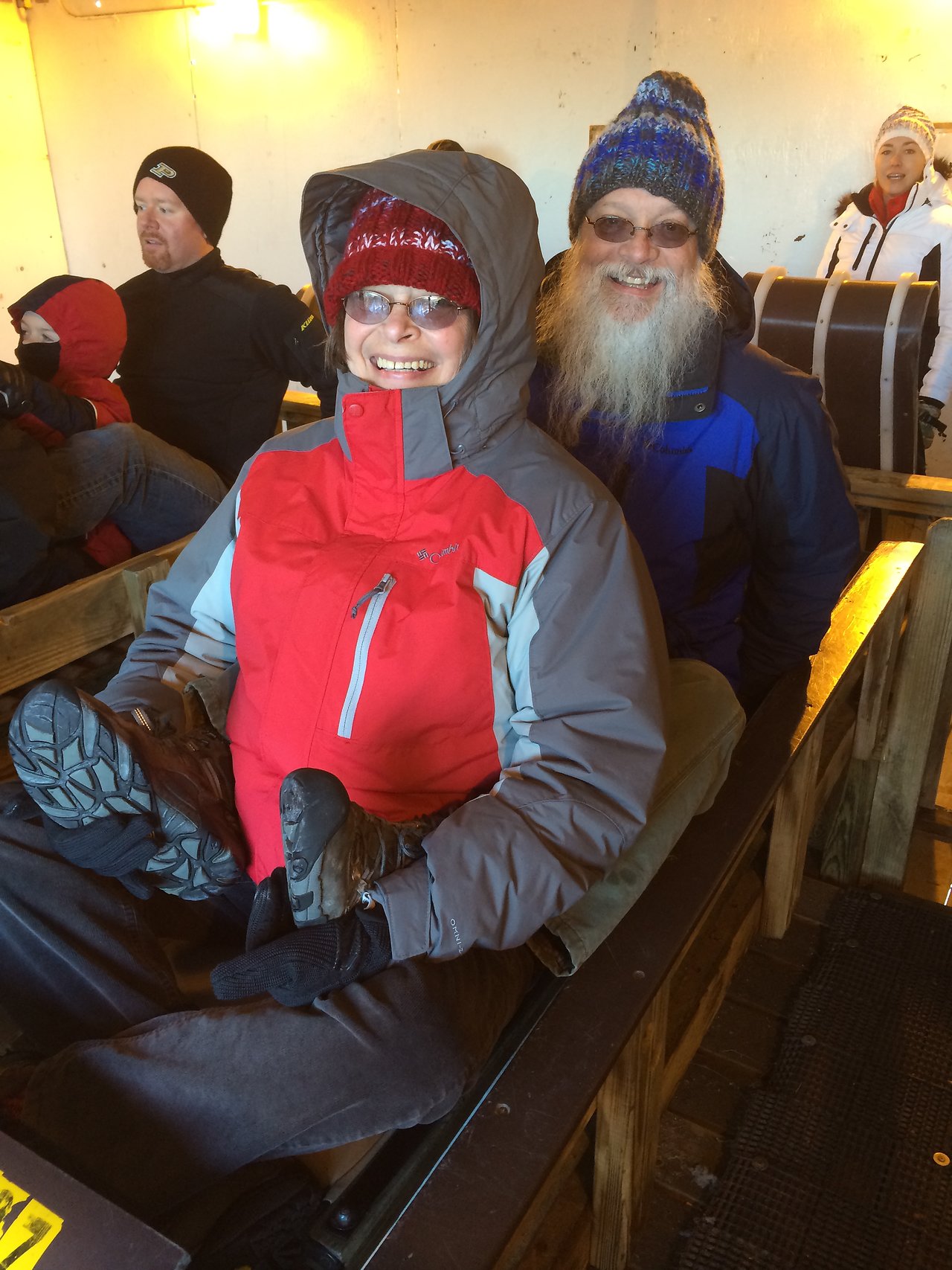Two people in winter clothing sit on a wooden sled, smiling.