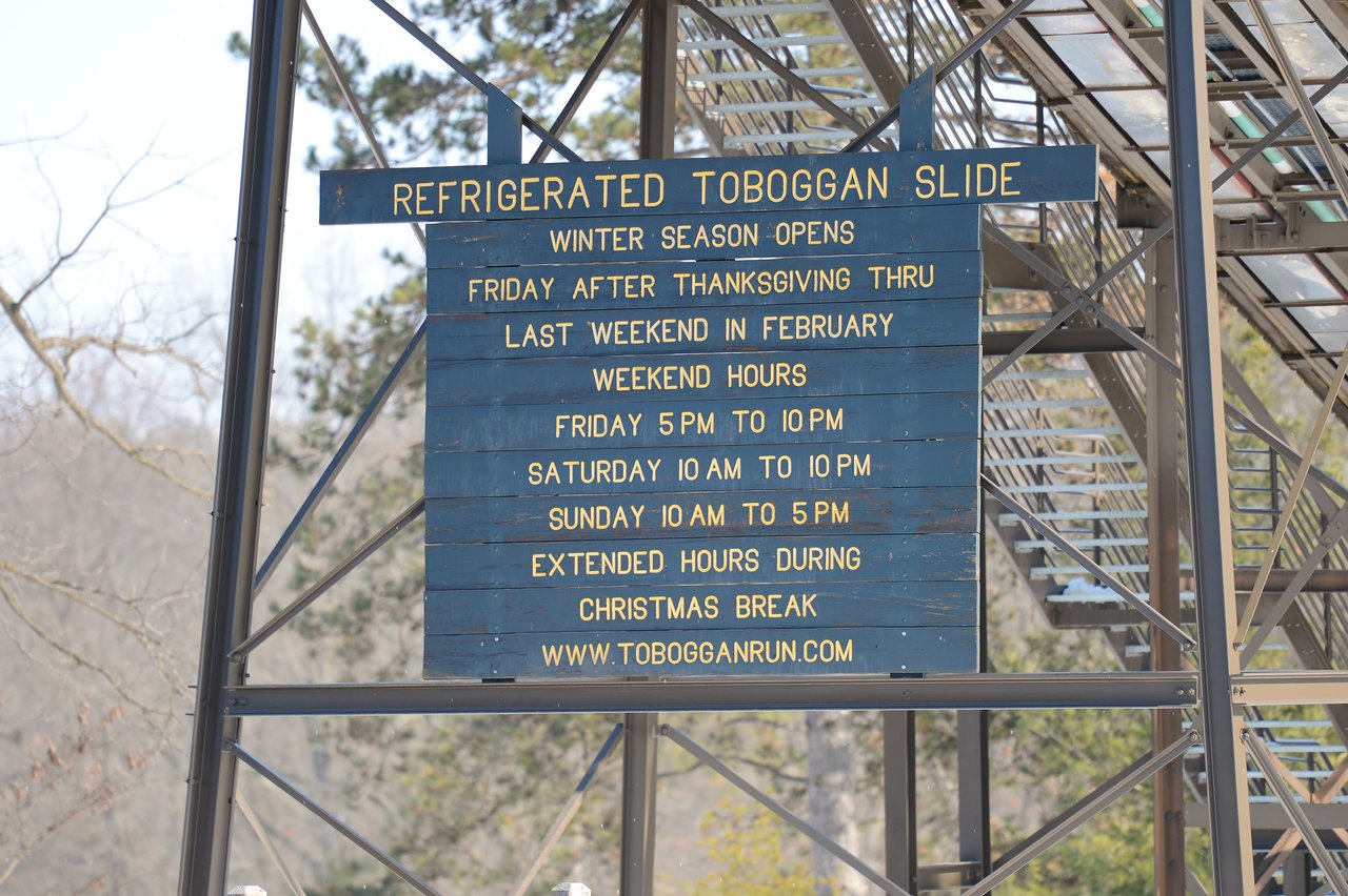A sign displays the operating hours for a refrigerated toboggan slide, open from late November to February weekends.