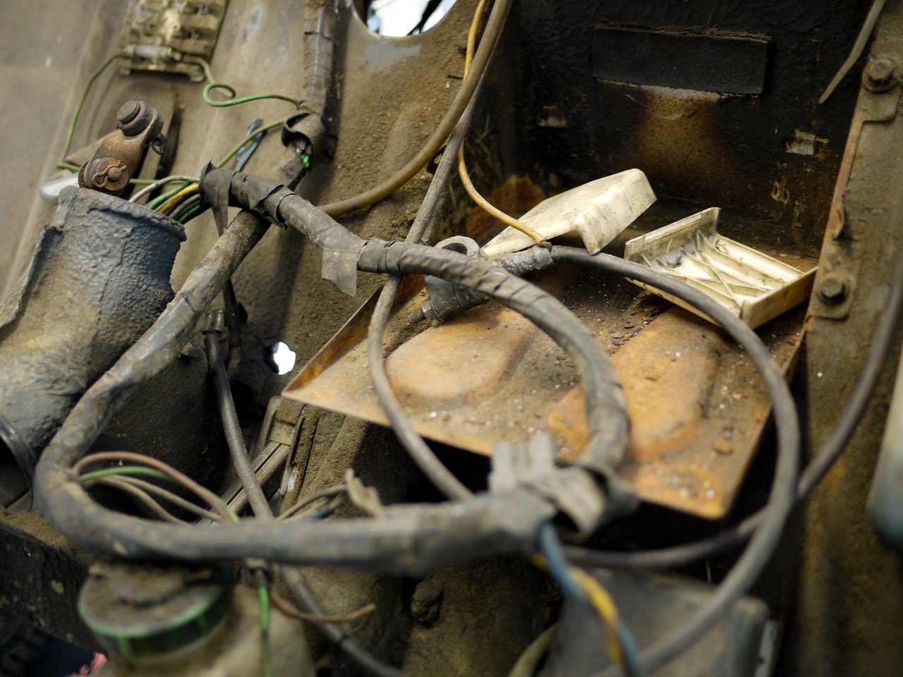 Close-up of a rusted mechanical area with tangled wires and an open, dirty cigarette pack resting on a metal surface.
