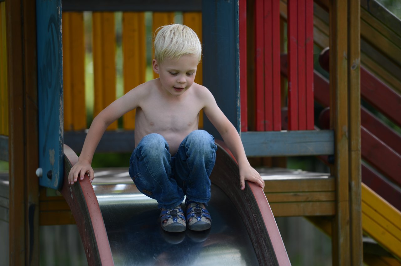 A young boy sits at the top of a slide, preparing to go down at a playground.