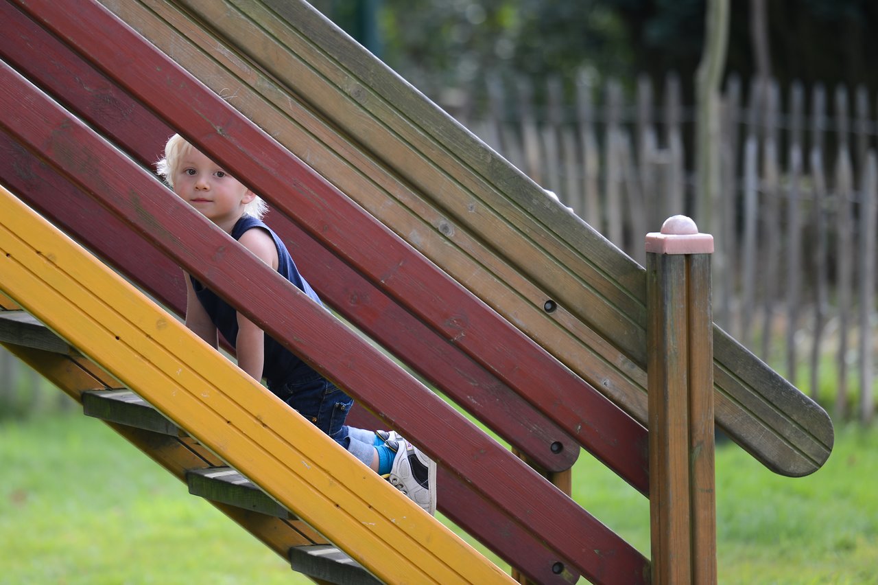 A young child climbs a wooden playground structure, looking towards the camera.