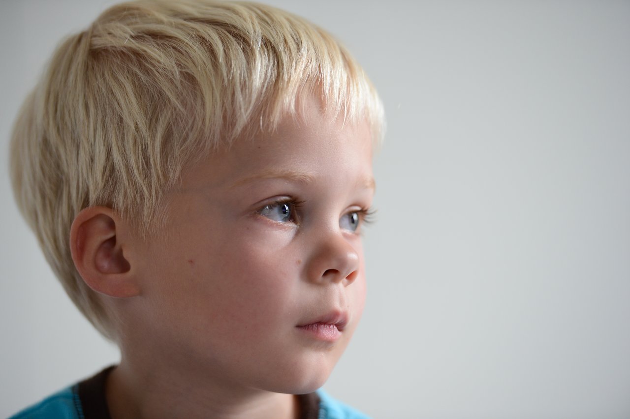 A young child with blonde hair watches something intently, appearing focused.