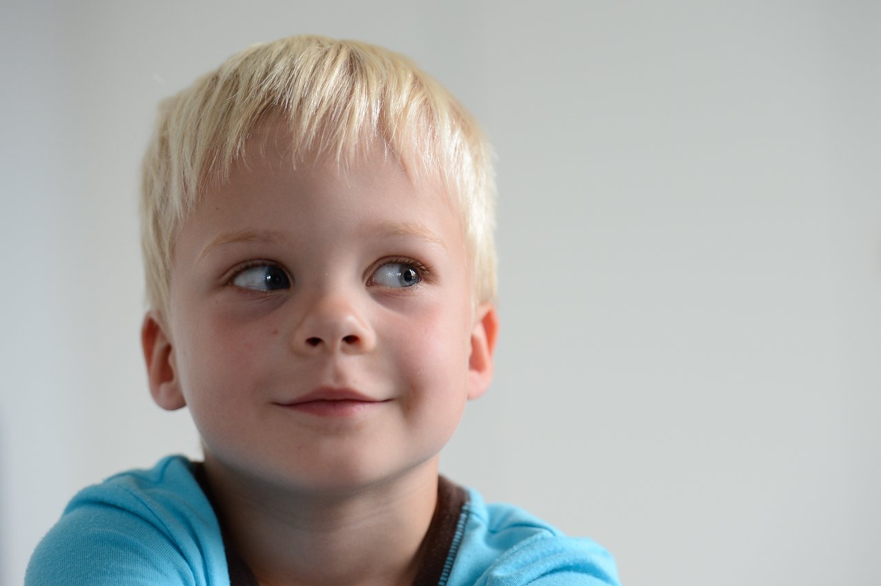 A young child in a blue shirt looks to the side with a curious expression.