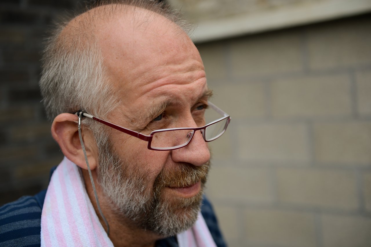 A man with glasses and a beard looks off to the side, wearing a striped towel over his shoulder.