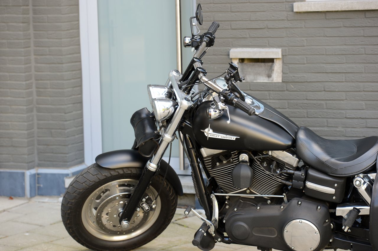 A black Harley-Davidson motorcycle is parked on a paved sidewalk next to a modern brick and glass building.