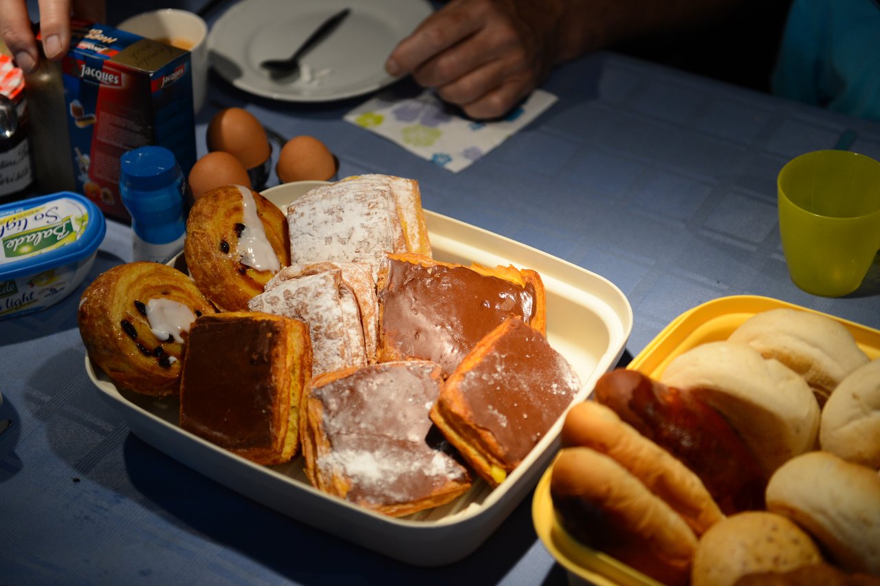 A tray of assorted pastries, including chocolate-covered and icing-topped ones, on a table set for breakfast.