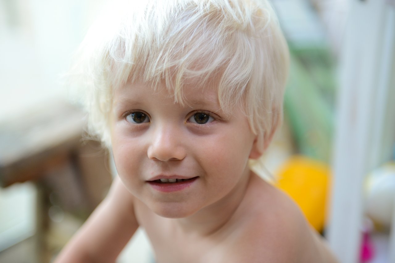 A young child with light blonde hair smiles while looking directly at the camera.
