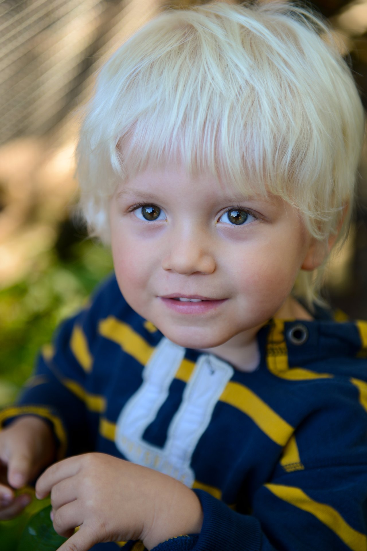 A young child with light blonde hair and a striped hoodie looks at the camera with a slight smile.